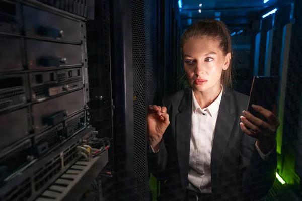 Pretty female administrator checking network connections in server room — Stock fotografie