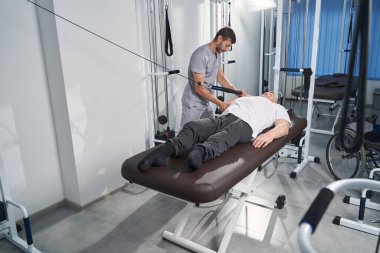 Adam masaj masasındaki direnç bandını fizyoterapistle çekiyor.