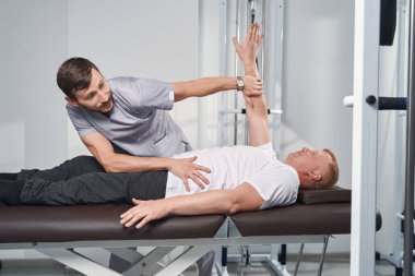 Doktor masaj masasında spor sakatlığı olan hastasını muayene ediyor.