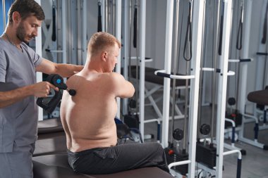 Fizyoterapist erkeğin omurgasını tedavi ediyor, masaj aleti ile geri dönüyor.