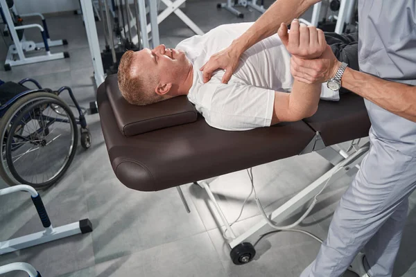 Close up man treats shoulder with physiotherapist on massage table — Stock Photo, Image