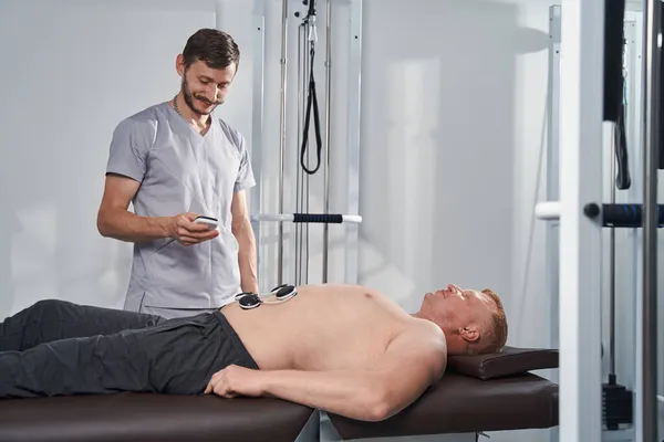 Doctor treats man with disability stomach with electrostimulator — Stock Photo, Image