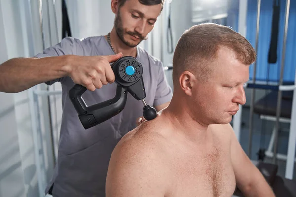 Spezialist massiert Rücken mit Schlagwerkzeug von Mann mit Behinderung — Stockfoto