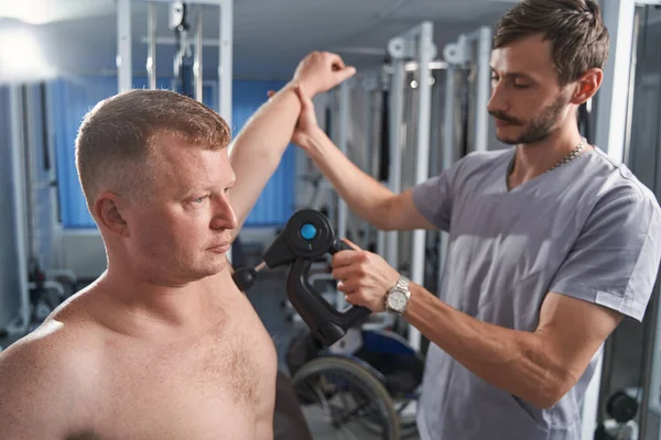 Physiotherapeut behandelt männliche Brustmuskulatur mit Massagepistole — Stockfoto