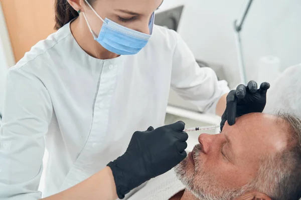 Cosmetologo in maschera medica fare iniezione in faccia all'uomo — Foto Stock