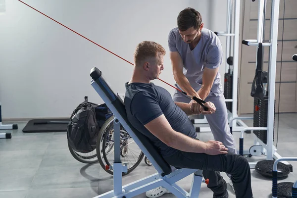 Mann mit Behinderung schnallt Gewichthebegerät mit Therapeut an — Stockfoto