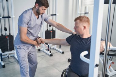 Kinezi terapisi egzersizi. Doktor omuz ağrısı olan tekerlekli sandalyeli adamı tedavi ediyor.