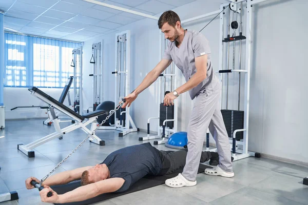 Trainer help young man training on pull cable exercising machine — Stock Photo, Image