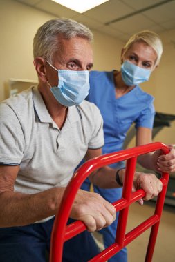 Olgun bir adam tıp merkezinde yürüyen çerçeve kullanır.