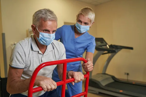 Fysiotherapeut die gehandicapte man leert walker te gebruiken in het herstelcentrum — Stockfoto
