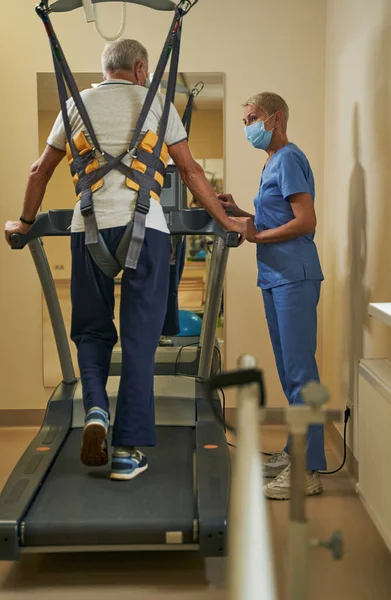 Зрелый мужчина использует беговую дорожку для ходьбы в реабилитационном центре — стоковое фото