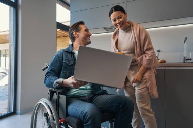 Belden aşağısı felçli neşeli bir adam ve karısı dizüstü bilgisayar izliyor.