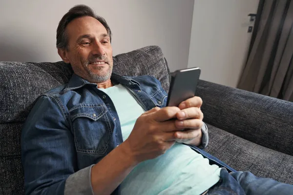 즐겁게 장성 한 남자 가집에서 스마트폰으로 문자 메시지를 보내다 — 스톡 사진