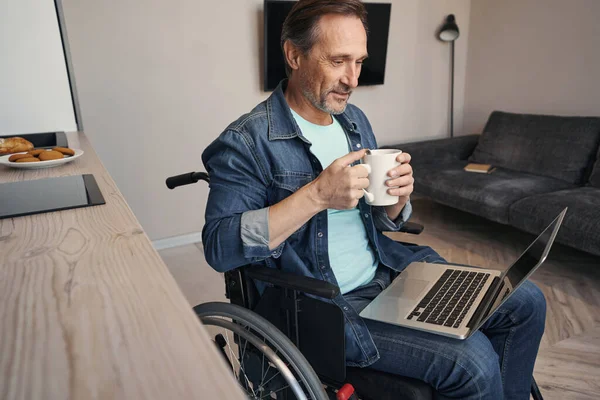Happy man with disability drinking coffee with laptop