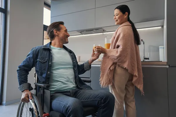Asyalı kadını önemseyen, tekerlekli sandalyedeki kocaya meyve suyu veren.