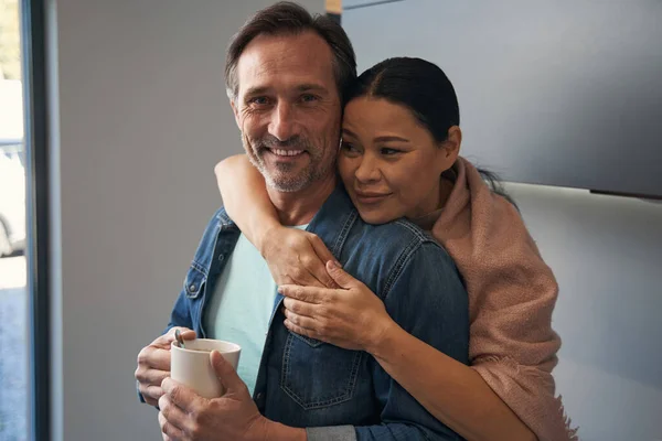 Feliz hombre maduro con taza de café en brazos de esposa — Foto de Stock