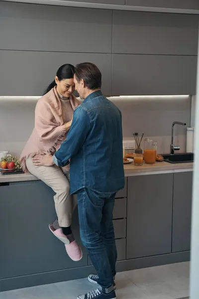 Amorosa pareja madura abrazándose durante la mañana en la cocina —  Fotos de Stock