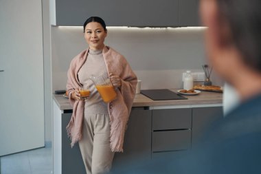 Gülümseyen Asyalı kadın kocası için meyve suyu hazırlıyor.