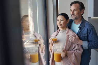 Mutlu çift evde pencerenin yanında sarılıyor.