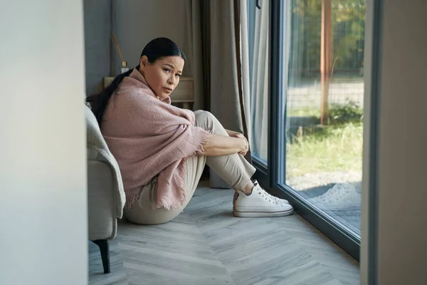 Sorglig asiatisk kvinna sitter på golvet hemma — Stockfoto