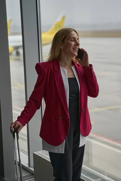 Lachende Frau nimmt Anruf auf Smartphone am Flughafen entgegen — Stockfoto