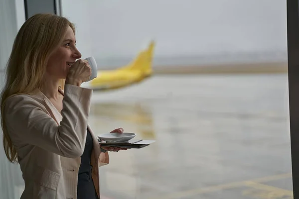 Путешественник пьет кофе из чашки возле окна бизнес-терминала — стоковое фото