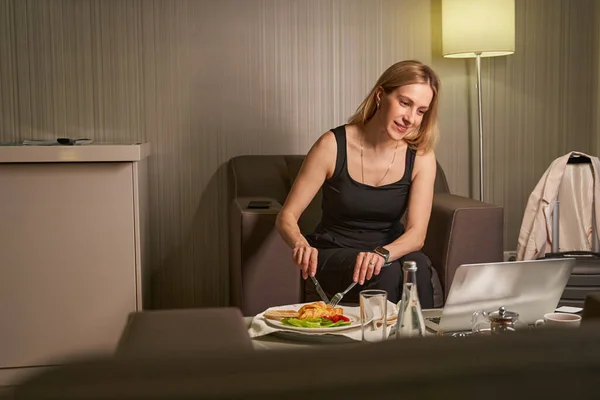 Weibchen essen Blätterteig mit Salat und starren auf Laptop — Stockfoto