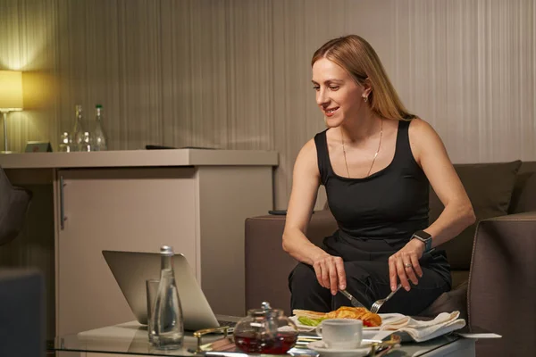 Женщина смотрит фильм на ноутбуке во время ужина в номере отеля — стоковое фото