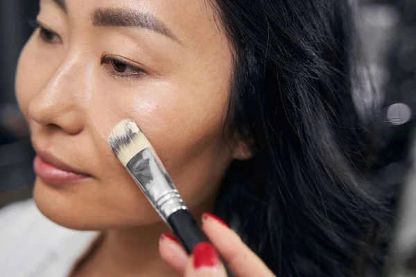 Mulher asiática elegante aplicando cosméticos faciais no salão — Fotografia de Stock