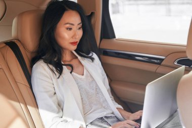 Dizüstü bilgisayarı olan güzel, zarif bir kadın bir otomobilin arka koltuğunda oturuyor.