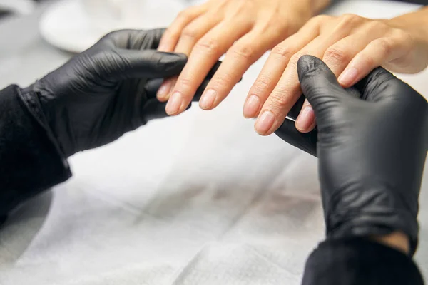 Maestro manicura en guantes negros está sosteniendo delgados y pulcros dedos —  Fotos de Stock