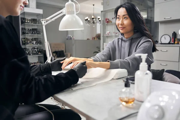 Encantadora hembra elegante con capucha gris consiguiendo manicura de uñas en el salón —  Fotos de Stock