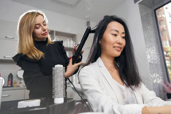 Affascinante signora elegante nel negozio di barbiere mentre un parrucchiere organizza i suoi capelli — Foto Stock