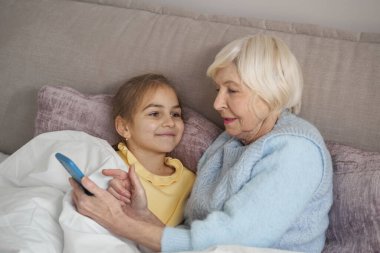 Küçük bir kızla akıllı telefon menüsünü araştıran odaklanmış yaşlı bir kadın.