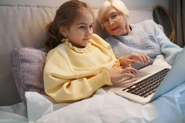 Бабушка и ребенок лежат в постели и смотрят на ноутбук — стоковое фото