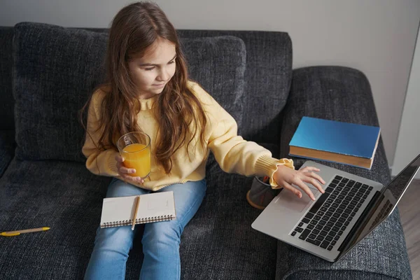 Focused girl holding glass of juice and using laptop — Stock Photo, Image