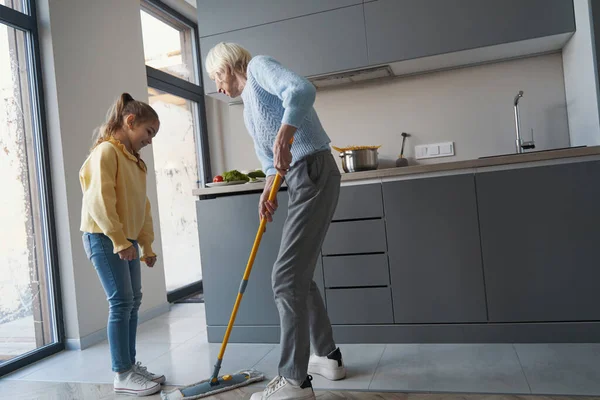 Mujer mayor y su nieta limpiando el suelo con una fregona — Foto de Stock