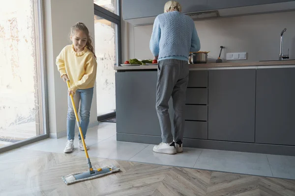 Cuidar a la niña limpiando el suelo mientras asiste a su abuela — Foto de Stock