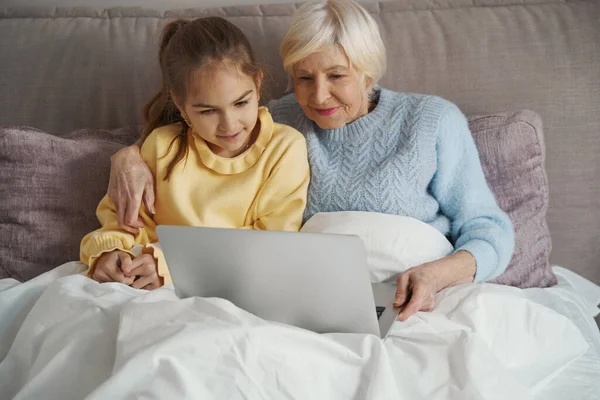 Расслабленная бабушка и ее внучка отдыхают и смотрят фильм — стоковое фото