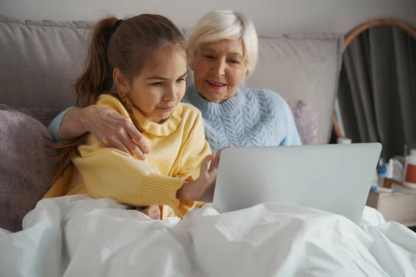 Зажатые пожилая женщина и маленькая девочка, глядя на ноутбук — стоковое фото