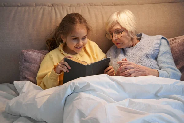 Radiante niña disfrutando de la cama historia tiempo con su abuela — Foto de Stock