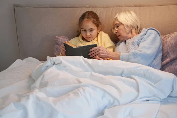 Бабушка и внучка вместе читают сказки на ночь — стоковое фото