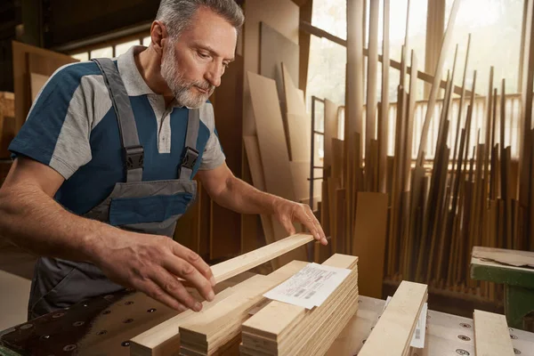 Attentive mature joiner putting wooden bar on pile — Foto Stock