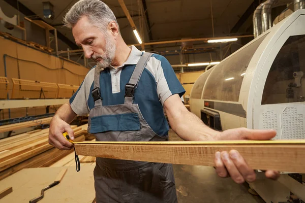 Attentive bearded man measuring length of wood — Zdjęcie stockowe