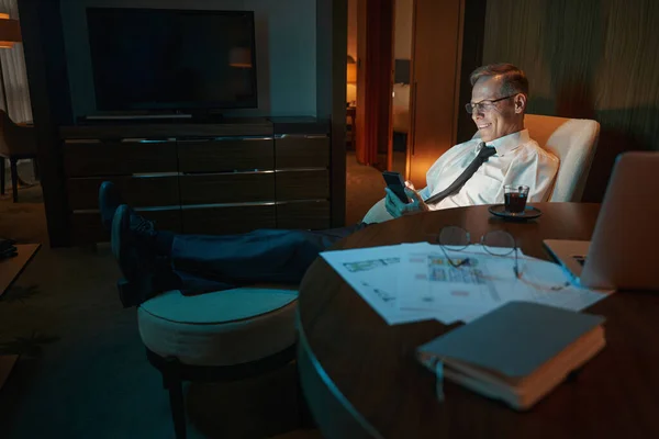 Mature businessman lying on armchair in dark hotel room — Stockfoto