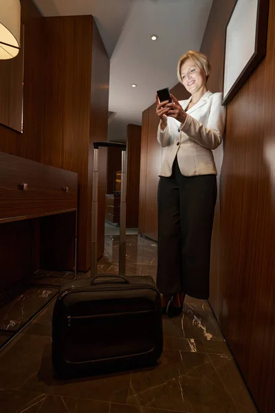 Businesswoman using smartphone standing in hallway of the hotel room — ストック写真