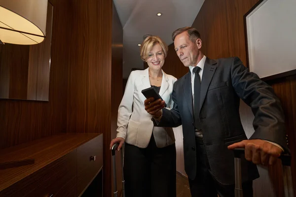 Business partners looking at phone in hallway of the hotel room — Stockfoto