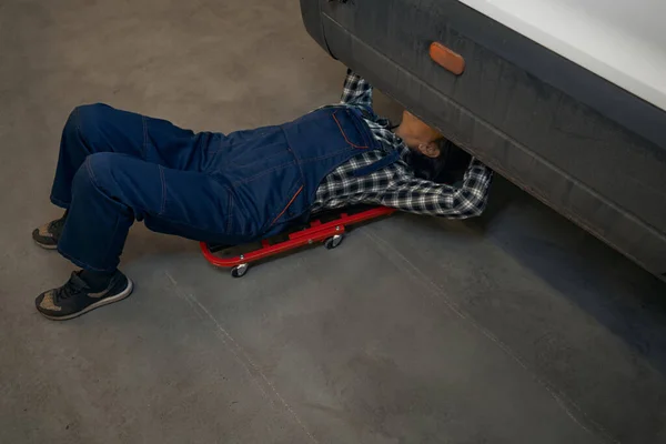 Skilled female car mechanic performing her job under the vehicle — Zdjęcie stockowe