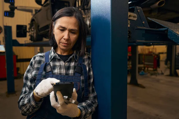 Worried female mechanic checking her phone updates at workplace — Stockfoto