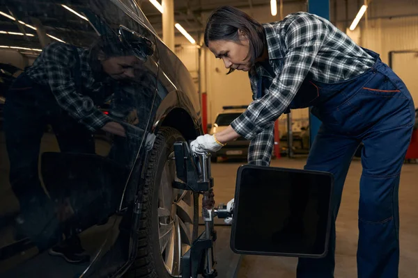 Capable woman working at car service station and replacing tyres — Stockfoto